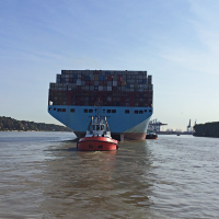 Foto eines Containerschiffs auf der Elbe vor dem Hamburger Hafen. Schlepper halten das riesige Schiff in der Fahrrinne.